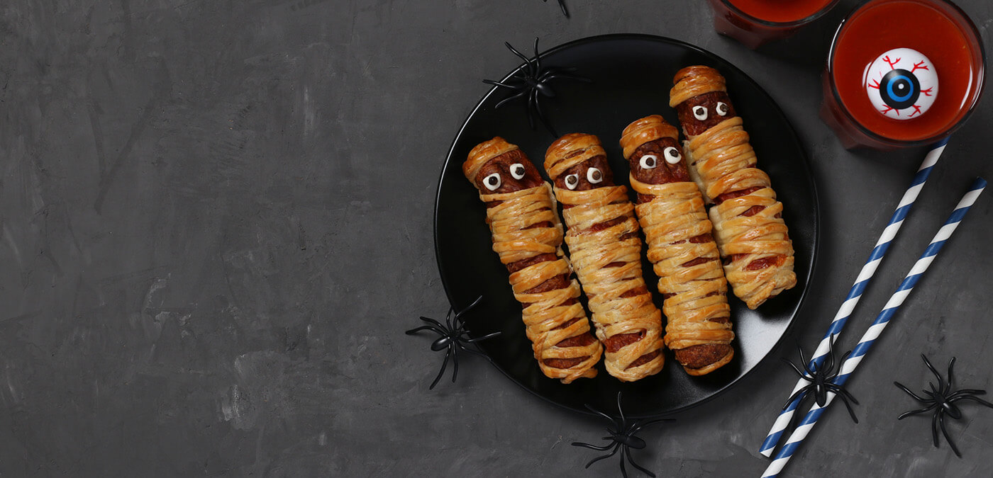 Sausages wrapped in dough to look like mummies on a black plate